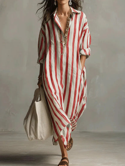 Red - A woman walks wearing an oversized, vertical-striped linen maxi dress in navy and white, featuring a collared V-neck, rolled-up sleeves, and side pockets, paired with a woven tote bag.