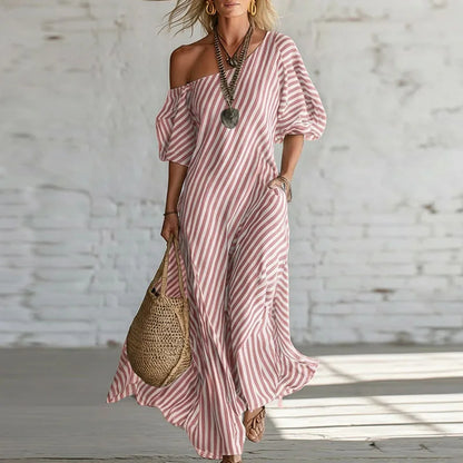 Pink - Woman wearing a long, striped, one-shoulder maxi dress with a puff sleeve and a side pocket, holding a woven tote bag.