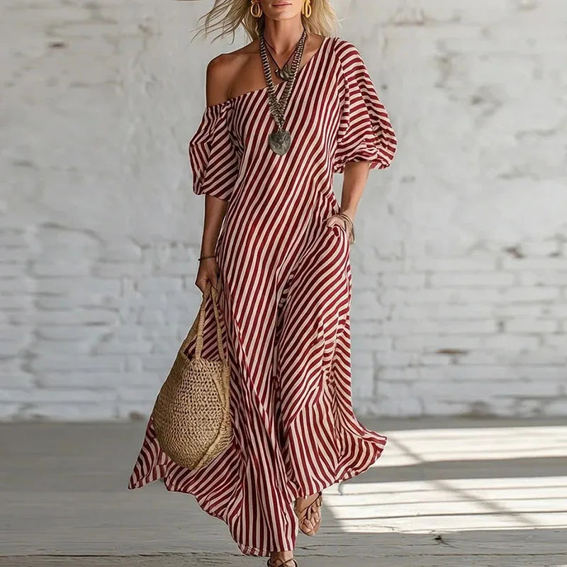 Red - Woman wearing a long, striped, one-shoulder maxi dress with a puff sleeve and a side pocket, holding a woven tote bag.