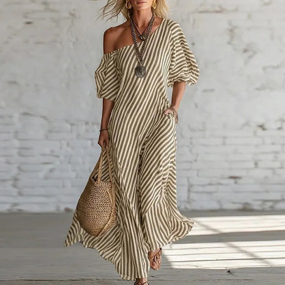 Khaki - Woman wearing a long, striped, one-shoulder maxi dress with a puff sleeve and a side pocket, holding a woven tote bag.