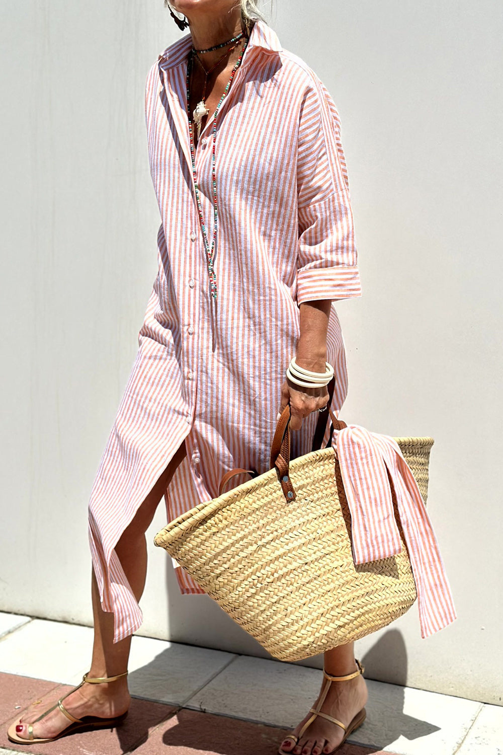 Woman walking outdoors wearing a striped poplin button-front midi dress with a collar and 3/4 sleeves, carrying a woven straw tote bag.
