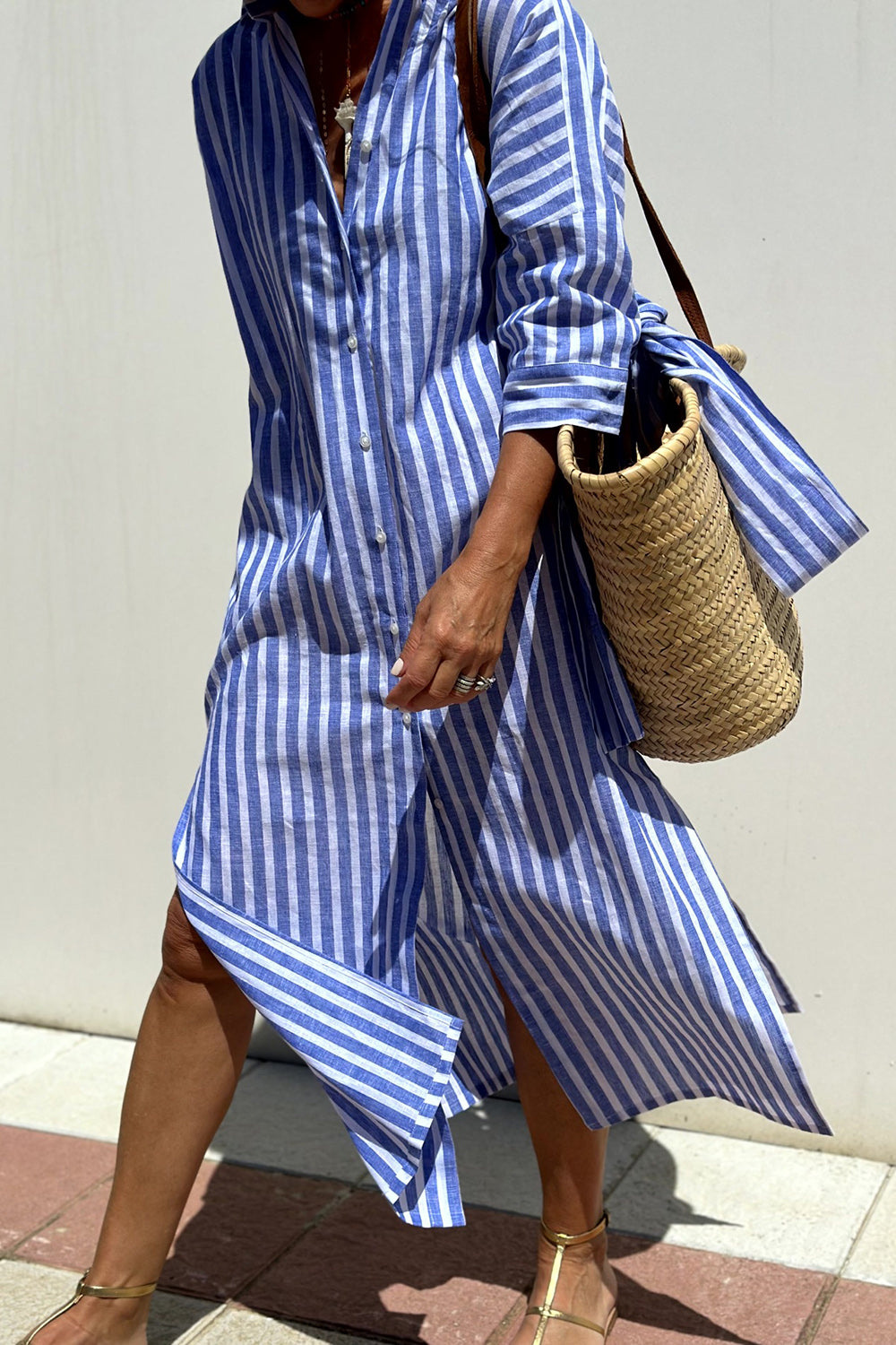 Blue - Woman walking outdoors wearing a striped poplin button-front midi dress with a collar and 3/4 sleeves, carrying a woven straw tote bag.