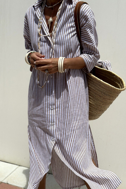 Blue - Woman walking outdoors wearing a striped poplin button-front midi dress with a collar and 3/4 sleeves, carrying a woven straw tote bag.