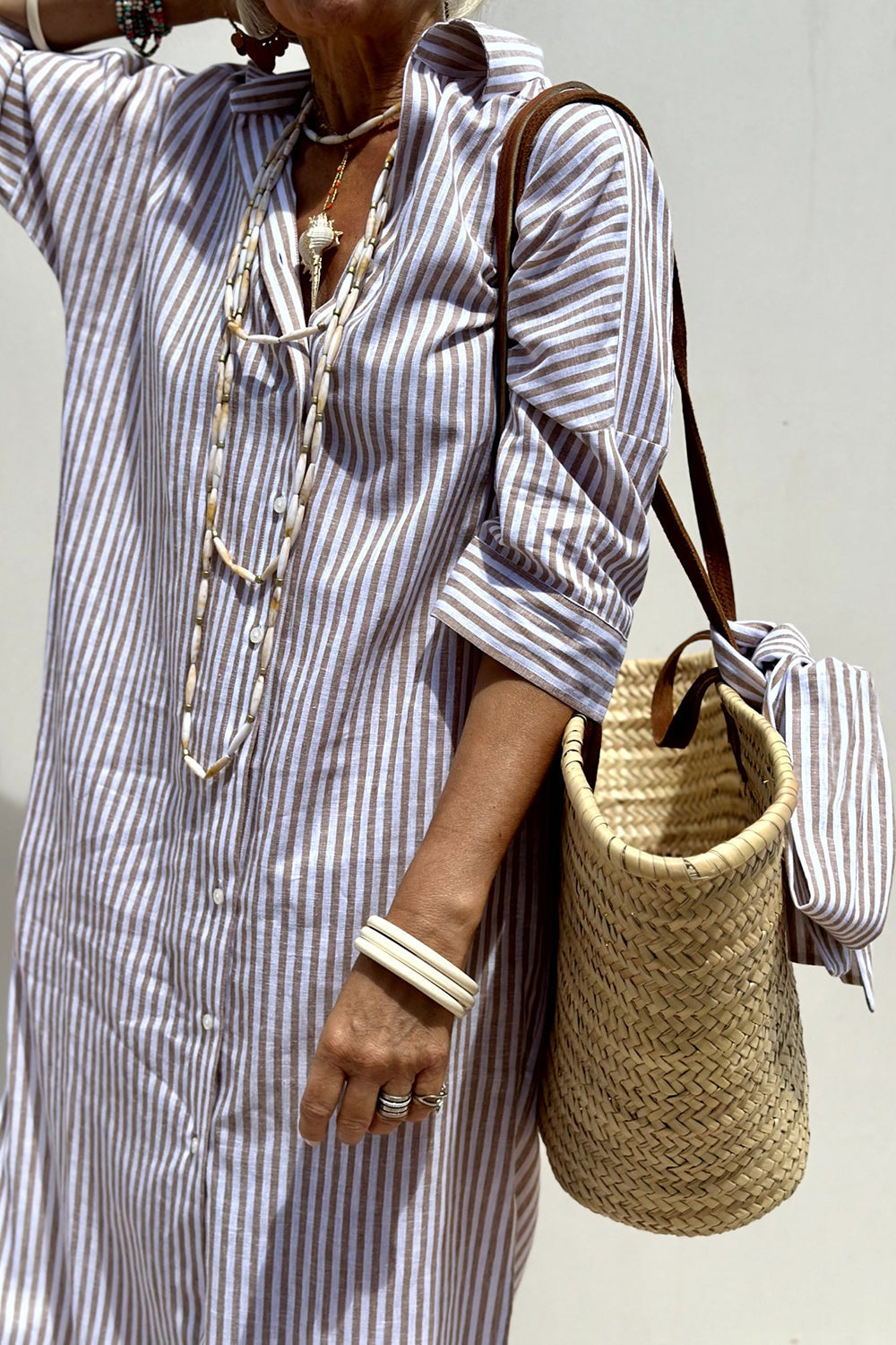 Khaki - Woman walking outdoors wearing a striped poplin button-front midi dress with a collar and 3/4 sleeves, carrying a woven straw tote bag.