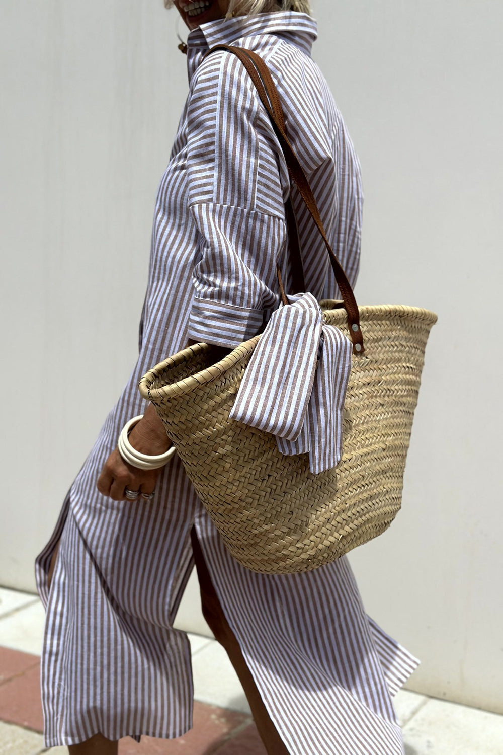 Khaki - Woman walking outdoors wearing a striped poplin button-front midi dress with a collar and 3/4 sleeves, carrying a woven straw tote bag.