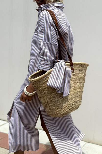 Khaki - Woman walking outdoors wearing a striped poplin button-front midi dress with a collar and 3/4 sleeves, carrying a woven straw tote bag.