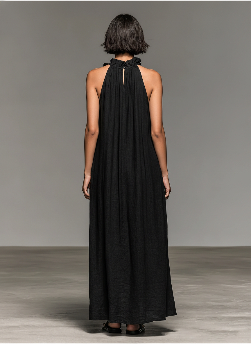 Black - Model walking in a sleeveless, textured maxi dress with a ruffled halter neckline, carrying a woven straw bag.