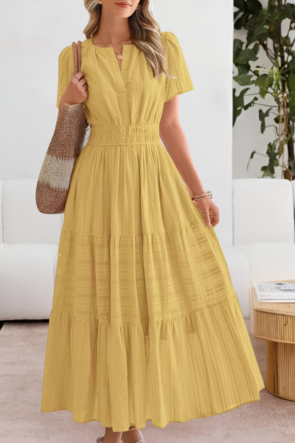 Yellow - A woman wearing a yellow textured cotton midi sundress with a smocked waist, split V-neckline, flutter sleeves, and a tiered skirt, holding a woven tote bag.