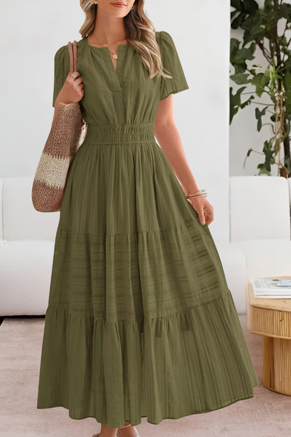 Green - A woman wearing a yellow textured cotton midi sundress with a smocked waist, split V-neckline, flutter sleeves, and a tiered skirt, holding a woven tote bag.