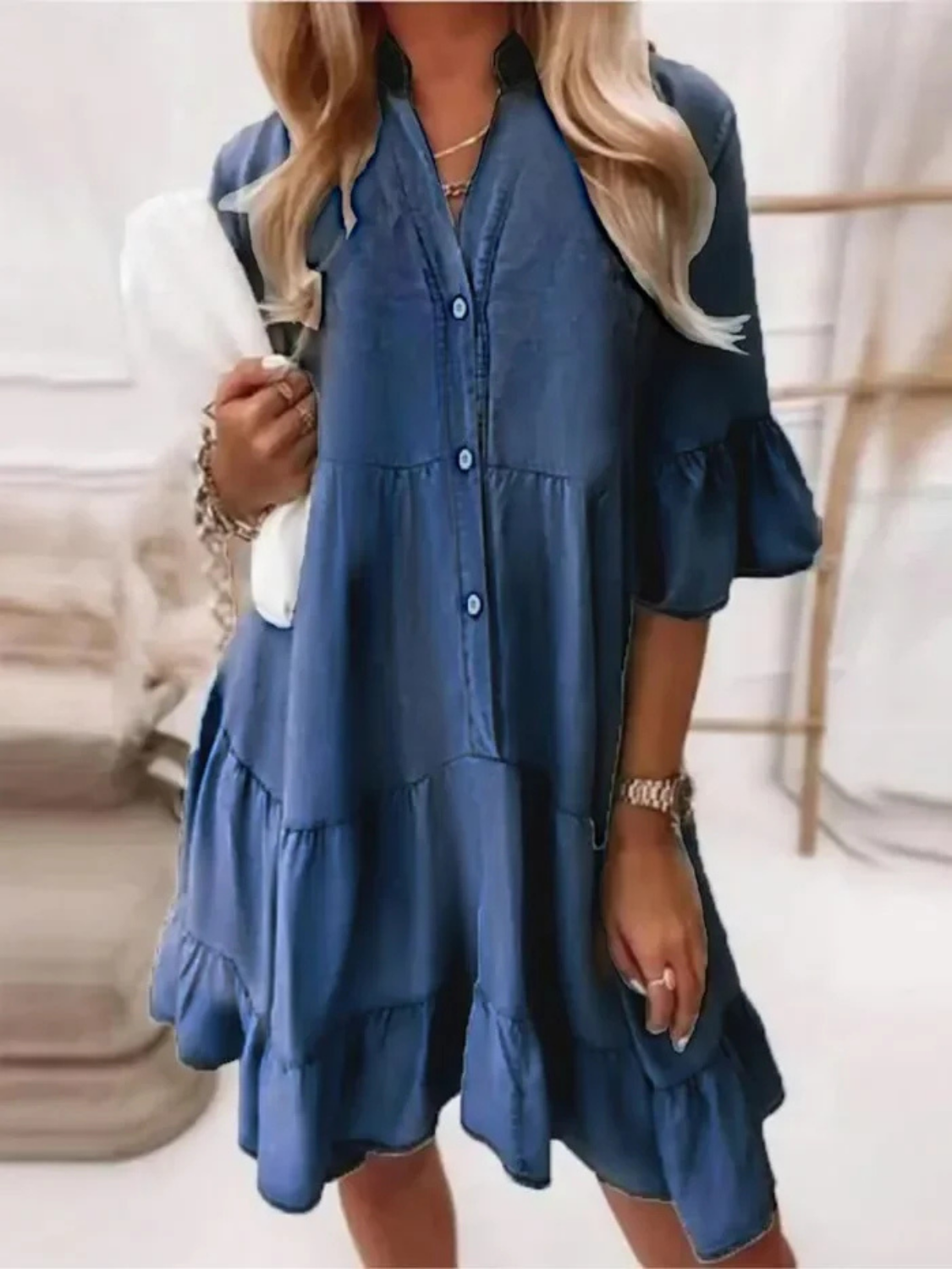 Dark Blue - Woman wearing a tiered denim babydoll mini dress with a button front, collar, and ruffle half sleeves, holding a small handbag.