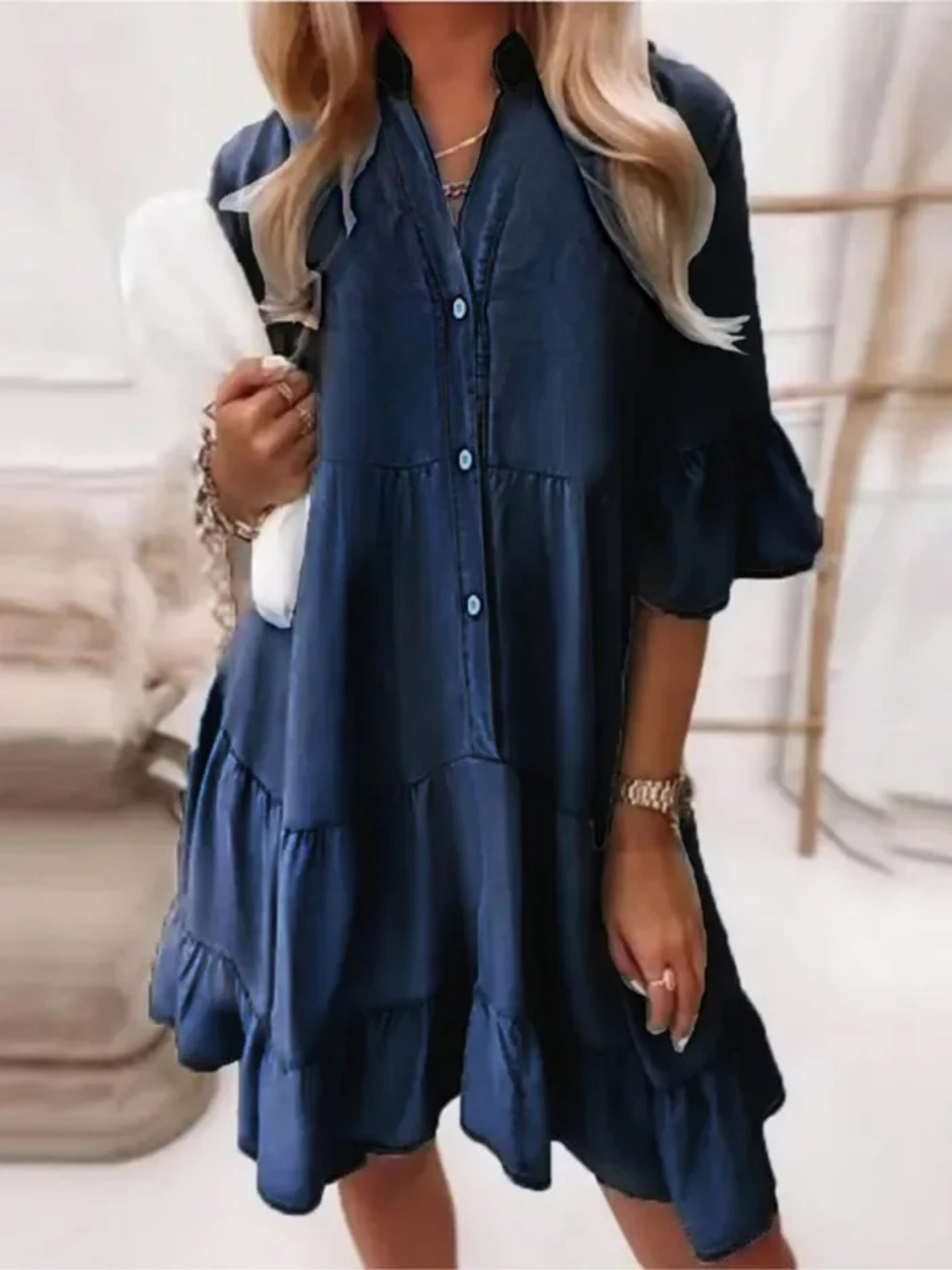 Navy - Woman wearing a tiered denim babydoll mini dress with a button front, collar, and ruffle half sleeves, holding a small handbag.