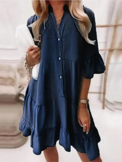 Navy - Woman wearing a tiered denim babydoll mini dress with a button front, collar, and ruffle half sleeves, holding a small handbag.