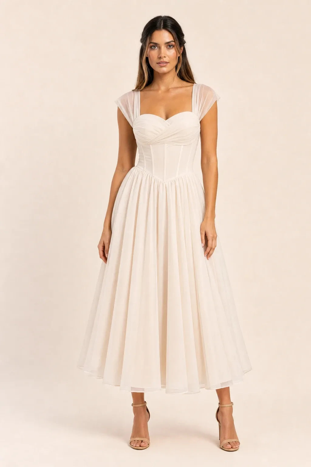 Apricot - Model wearing a romantic midi dress featuring a ruched sweetheart neckline, sheer cap sleeves, structured corset bodice with visible boning, and a full layered tulle skirt, standing indoors near a sunlit window.