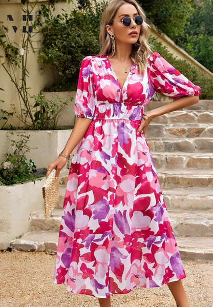 Pink - A woman wearing a vibrant, multicolored abstract floral print chiffon midi sundress with puff sleeves, a V-neckline, and a smocked waist, holding a woven straw clutch.