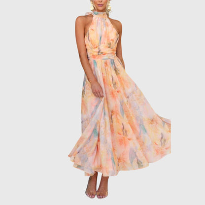 Premium - A woman wearing a sleeveless halter-neck maxi dress made of flowy watercolor chiffon in pastel orange, yellow, and blue shades, featuring a ruched waistband and a pleated A-line skirt.