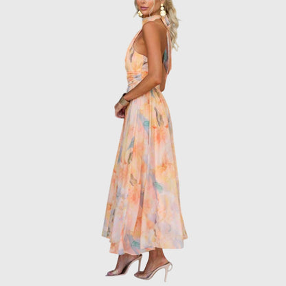 Premium - A woman wearing a sleeveless halter-neck maxi dress made of flowy watercolor chiffon in pastel orange, yellow, and blue shades, featuring a ruched waistband and a pleated A-line skirt.