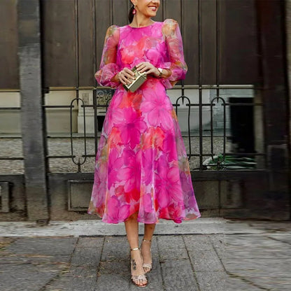 Pink - A woman wearing a vibrant pink and magenta watercolor floral chiffon midi dress with sheer puff sleeves, a crew neck, and an A-line skirt, paired with metallic heels.