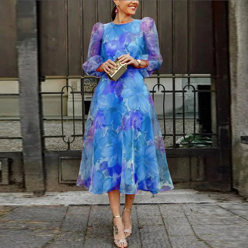 Blue - A woman wearing a vibrant pink and magenta watercolor floral chiffon midi dress with sheer puff sleeves, a crew neck, and an A-line skirt, paired with metallic heels.