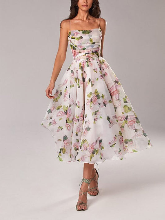 Pink - A woman wearing a white organza midi dress with a pink and green watercolor floral print, featuring spaghetti straps, a structured corset bodice with sheer waist detailing, and a voluminous A-line skirt.