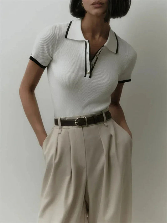 Woman wearing white ribbed knit polo shirt with brown belt and beige trousers