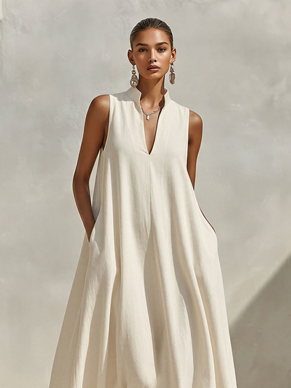 Cream - A model wearing a voluminous, sleeveless woven maxi dress with a deep V-neck and stand collar, standing outdoors.
