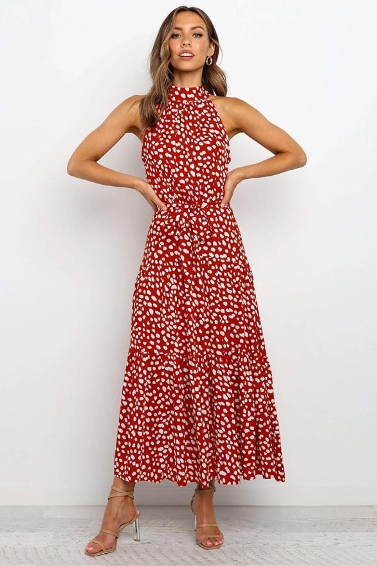Woman wearing a spotted halter neck maxi dress with a tie waist and tiered skirt.