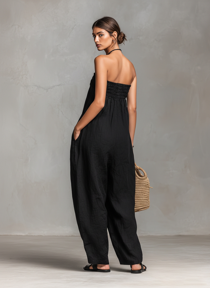 Black - Model wearing a strapless wide-leg jumpsuit with a ruched bodice, front tie detail, and side pockets, holding a woven bag.