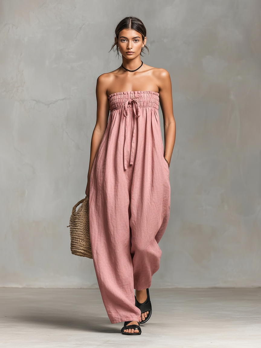 Light Pink - Model wearing a strapless wide-leg jumpsuit with a ruched bodice, front tie detail, and side pockets, holding a woven bag.