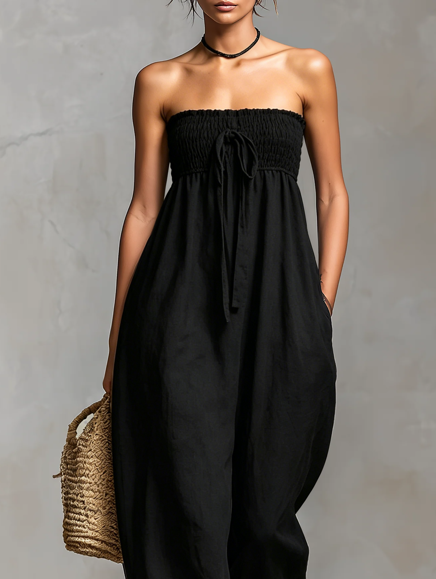 Light Pink - Model wearing a strapless wide-leg jumpsuit with a ruched bodice, front tie detail, and side pockets, holding a woven bag.